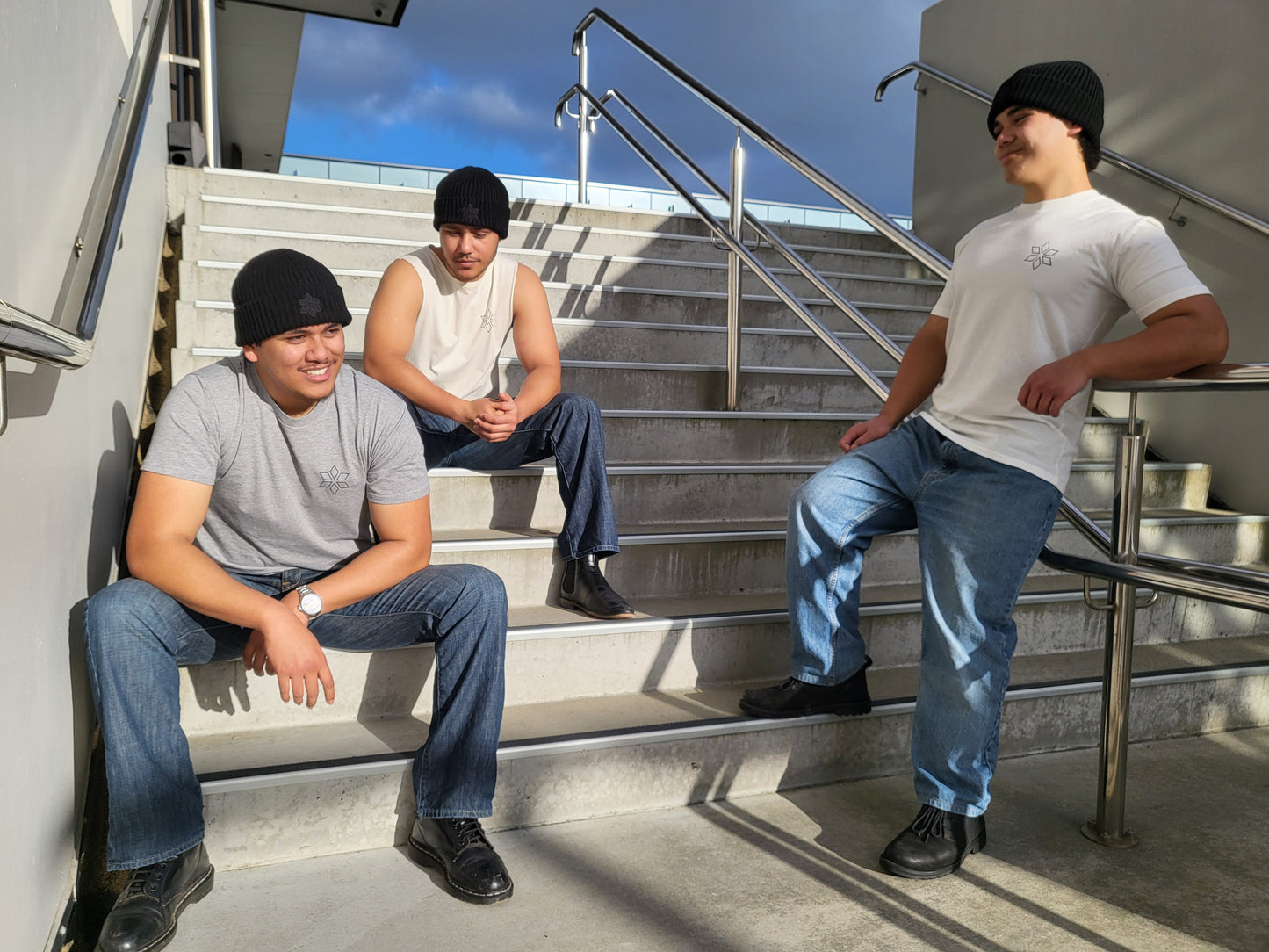 Group of men wearing black beanies sitting on concrete stairs, wearing clothing from HUA Clothing brand