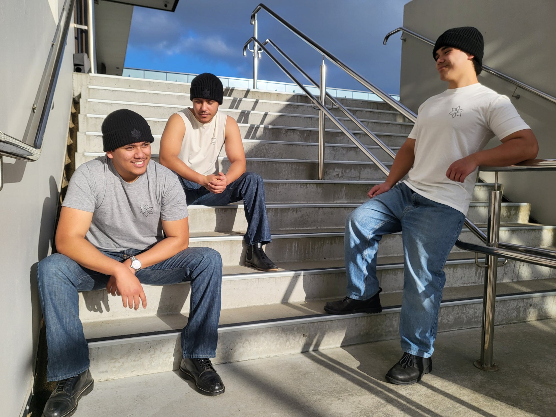 Group of men wearing black beanies sitting on concrete stairs, wearing clothing from HUA Clothing brand