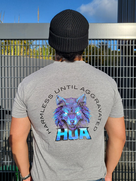 A man viewed from behind wearing a gray t-shirt with a large graphic on the back. The graphic features a glowing blue and purple wolf head with the text 'HARMLESS UNTIL AGGRAVATED' arched above and 'HUA' below.