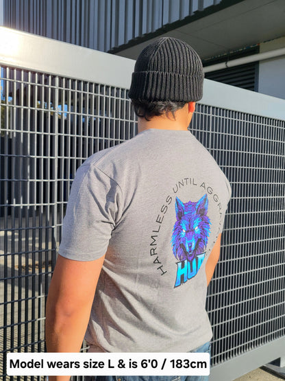 A man wearing a gray t-shirt with a large blue and purple wolf graphic on the back, paired with a black beanie, standing in front of a metal fence.